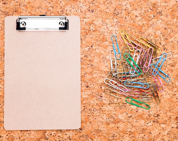 Free photo clipboard and multicolored paper clips on cork background