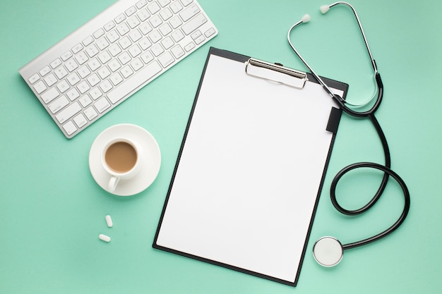 Free photo clipboard; wireless keyboard; cup of coffee and stethoscope on green desk