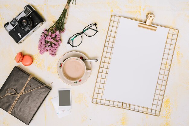 Clipboard with coffee, camera and flowers bouquet on table