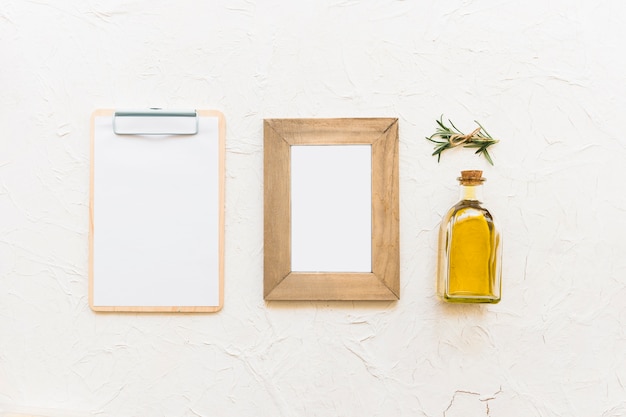 Free photo clipboard and wooden frame with oil bottle and rosemary herb