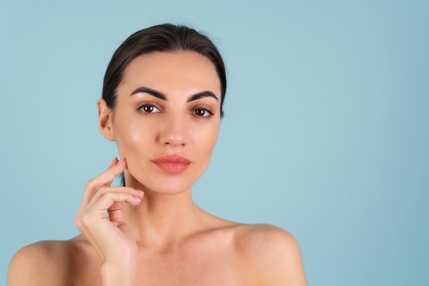 Close beauty portrait of a topless woman with perfect skin and natural make-up, plump nude lips, on a blue background