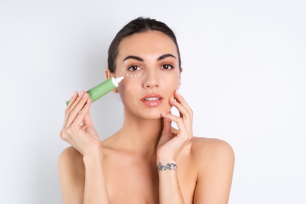 Close beauty portrait of a topless woman with perfect skin and natural makeup holding a cream for moisturizing and elasticity of the skin under the eyesx9