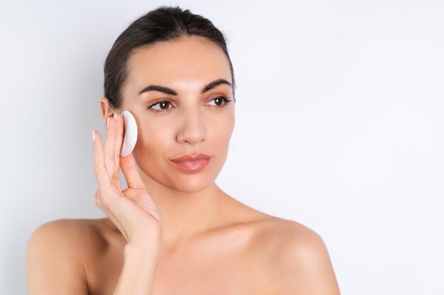 Close beauty portrait of a topless woman with perfect skin and natural makeup removing cotton pads on a white backgroundx9