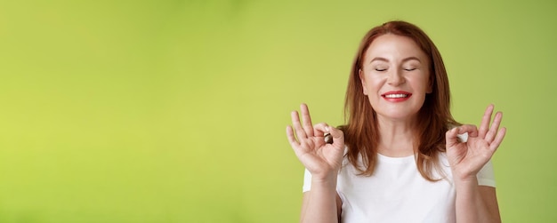 Free photo close to perfection closeup peaceful relaxed redhead happy woman closed eyes pure delighted smile show zen peace satisfaction gesture meditating reach nirvana calm stand green background