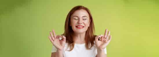 Free photo close to perfection closeup peaceful relaxed redhead happy woman closed eyes pure delighted smile show zen peace satisfaction gesture meditating reach nirvana calm stand green background