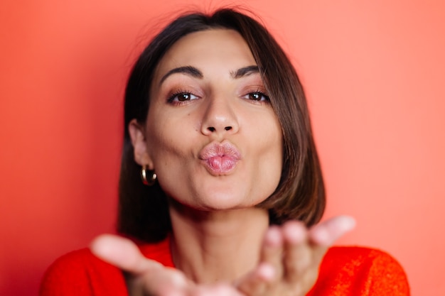 Free photo close portrait of woman on red wall looks to front and sends air kiss