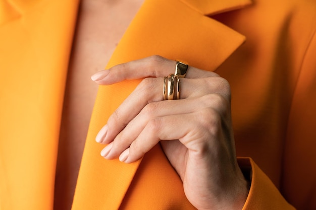 Free Photo close shot of a thin graceful hand of a girl with a nude spring trendy manicure and a gold ring on her fingers in an orange jacket