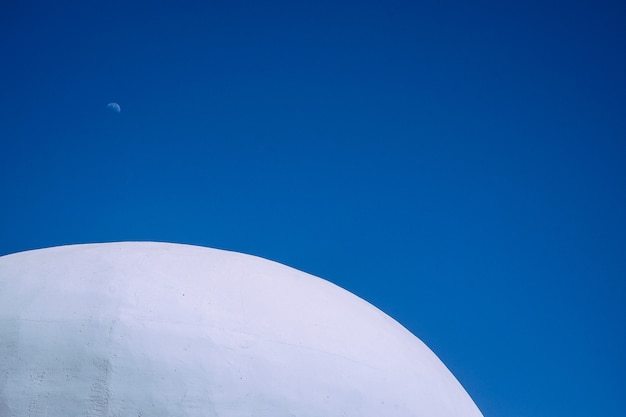 Close shot of the top of the white concrete round building with clear blue sky in the background