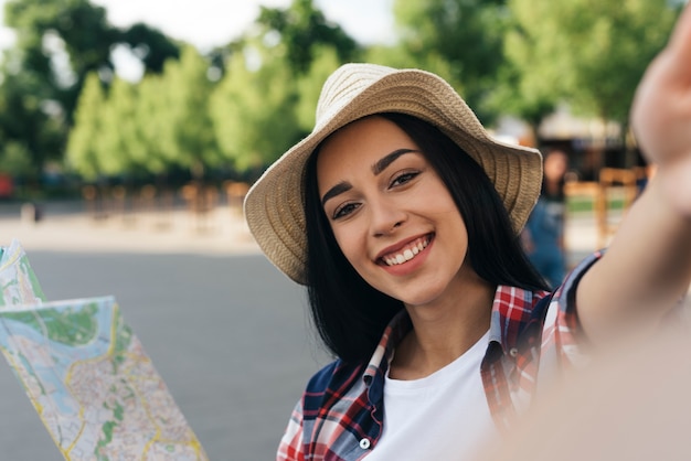 Free Photo close-u of smiling woman holding map and taking selfie at outdoors