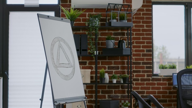 Close up of aa meeting sign on white board in therapy session space with chairs in circle. Office with furniture and anonymous alcoholics symbol used for rehabilitation program.