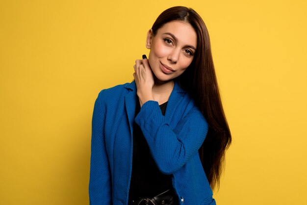 Close up  adorable lovely woman in blue jacket posing with smile over yellow wall. European female model posing