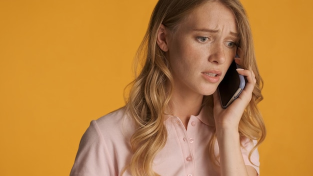 Close up afraid blond woman emotionally talking on phone isolated on colorful background Worry expression