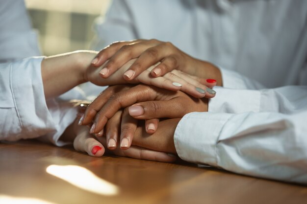 Close up of african-american and caucasian human's hands holding on wooden table