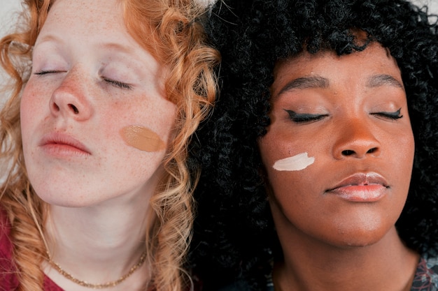 Free Photo close-up of an african and caucasian woman's face with skin tone foundation cream on cheek