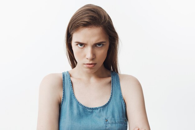 Close up of agresive attractive young caucasian woman with dark long hair in blue shirt  with angry face expression,