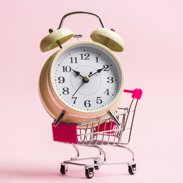 Close-up of an alarm clock on trolley over pink background