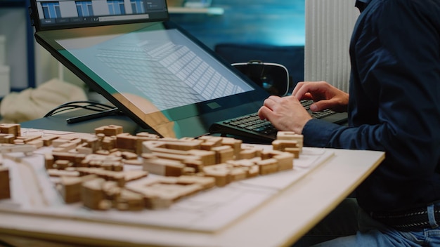 Free photo close up of architect hands using touch screen computer and maquette on table. man engineer working with technology to analyze building model for construction layout and development