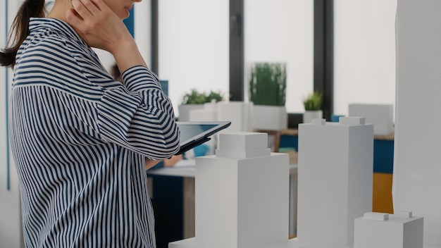 Free photo close up of architect holding tablet and analyzing building model to plan layout. woman engineer using digital device to design construction structure and development project.