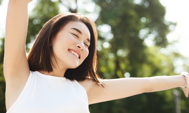 Close-up of asian woman stretching hands up and smiling, walking in park, looking carefree and happy