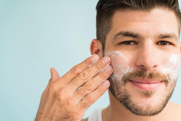 Close-up of attractive male grooming himself with skincare cream on cheeks  in studio