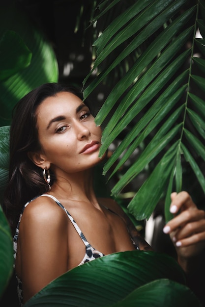 Free photo close up of attractive young woman with perfect tan wearing bikini posing in tropical jungle palm leaves with sensual smile female tourist relaxing on vacation