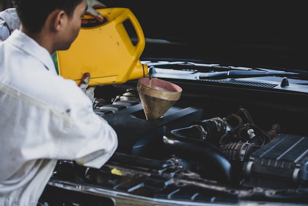 Close up Auto mechanic hand pouring and replacing fresh oil into car engine at auto repair garage. Automobile maintenance and industry concept