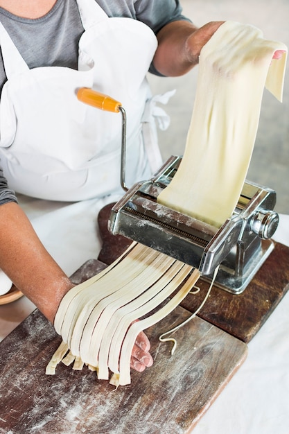 Free Photo close-up of baker cutting raw dough into tagliatelle on pasta machine