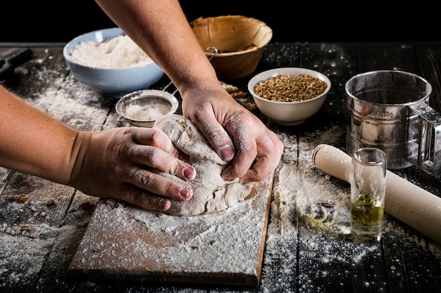 Close-up of baker's kneading the dough on chopping board with ingredients