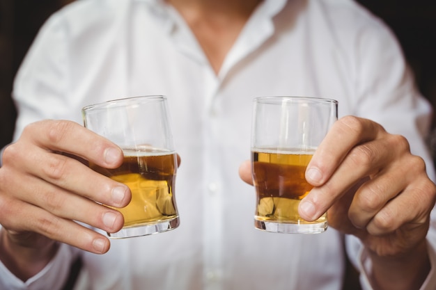 Close-up of bartender holding whisky shot glasses at bar counter