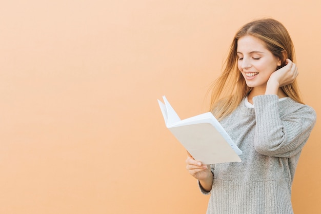 Close-up of beautiful young woman reading book against colored backdrop