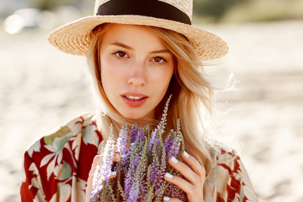 Close up beauty portrait of lovely romantic blond girl  enjoying perfect smell of lavender. Skincare and cosmetic concept. Warm sunset colors.