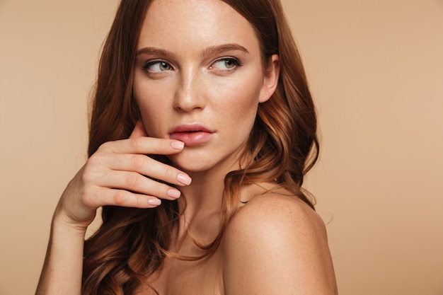 Free photo close up beauty portrait of mystery ginger woman with long hair posing sideways while looking away