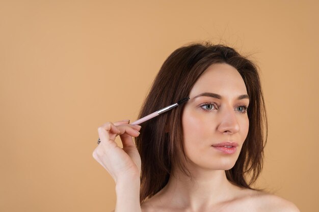 Close up beauty portrait of a woman with perfect skin and natural makeup, shiny lips, holding an eyebrow brush