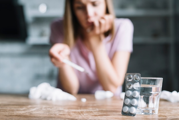 Free photo close-up of blister pack and glass of water with sick woman in background