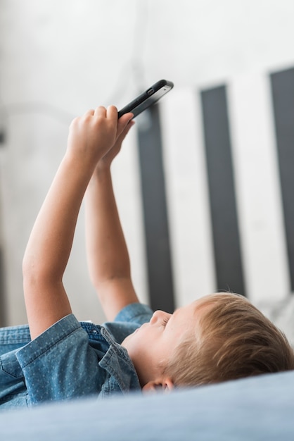 Close-up of blonde boy lying on bed using mobile phone