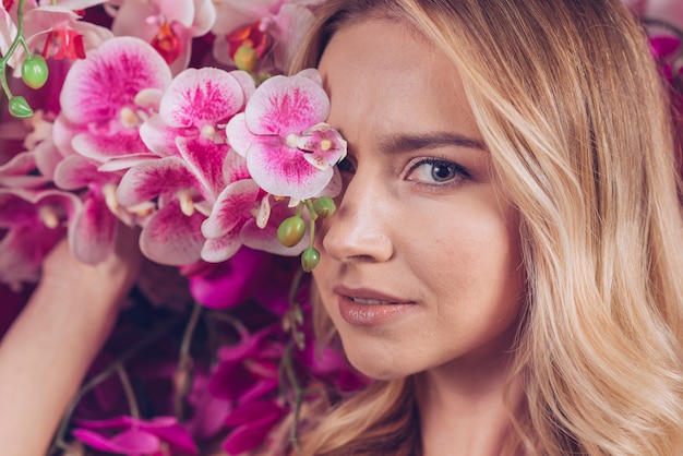 Free Photo close-up of blonde young woman covering her one eyes with pink orchid