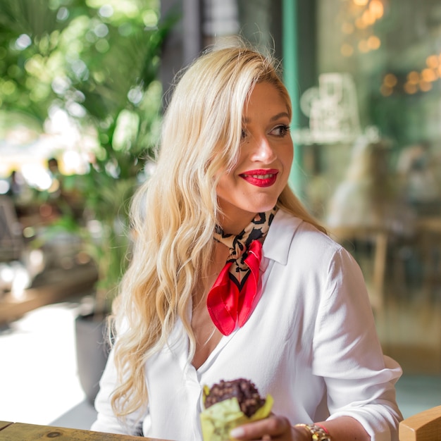 Close-up of blonde young woman holding muffin in the hand