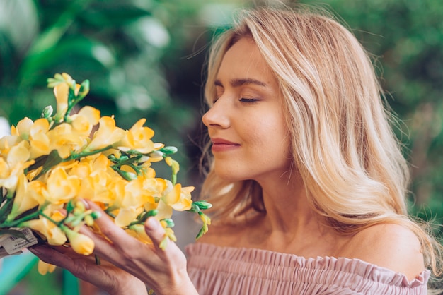 Free photo close-up of a blonde young woman smelling the freesia flowers