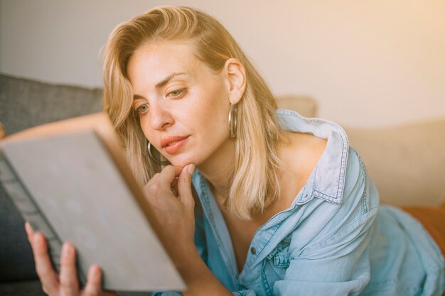 Close-up of blonde young woman with hand on chin reading the book