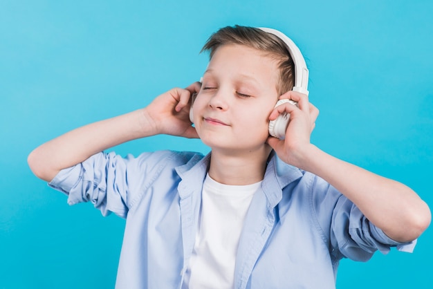 Free Photo close-up of a boy enjoying listening music on white headphone against blue backdrop