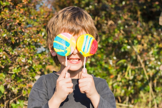 Close-up of boy holding two lollipops in front of his eyes