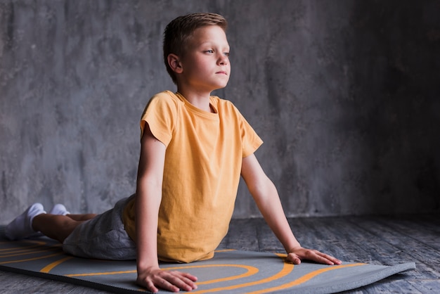 Free photo close-up of a boy stretching on exercise mat in front of concrete wall