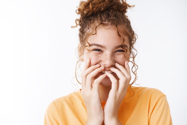 Close-up bright emotive happy young smiling redhead girl messy hairbun laughing cover mouth chuckling during important serious meeting cannot hold grin, standing excited playful white background