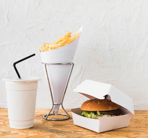 Free photo close-up of burger; french fries and disposal cup on wooden desk