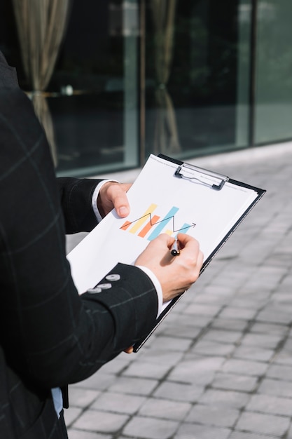 Free photo close-up of business person's hand drawing increasing arrow on graph over the clipboard