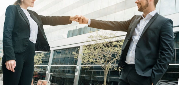 Free Photo close-up of businessman and businesswoman standing in front of building bumping fist