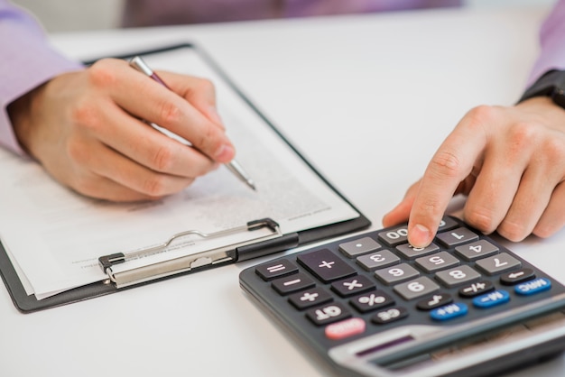 Close-up Of Businessman Calculating Invoices Using Calculator