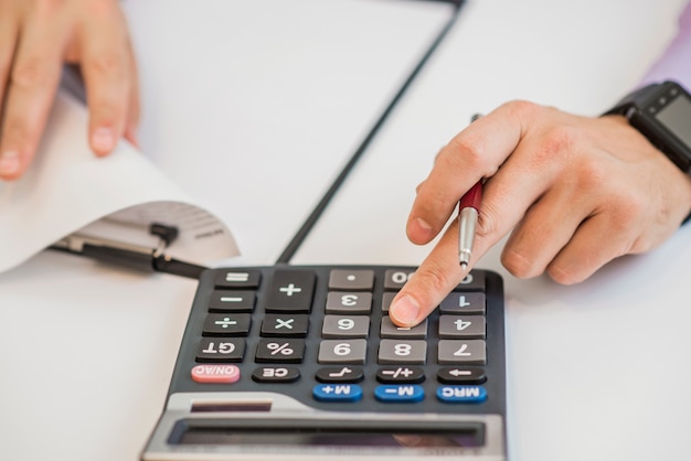 Close-up Of Businessman Calculating Invoices Using Calculator