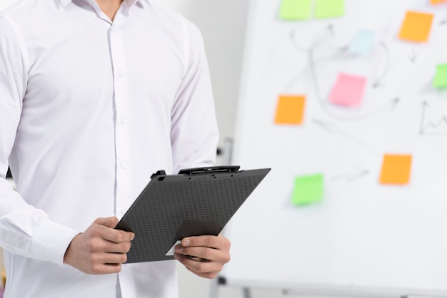 Free photo close-up of a businessman holding black clipboard in hand standing near the flipchart