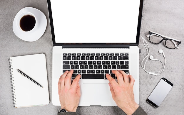 Close-up of a businessman's hand typing on digital tablet with office supplies and coffee cup on desk